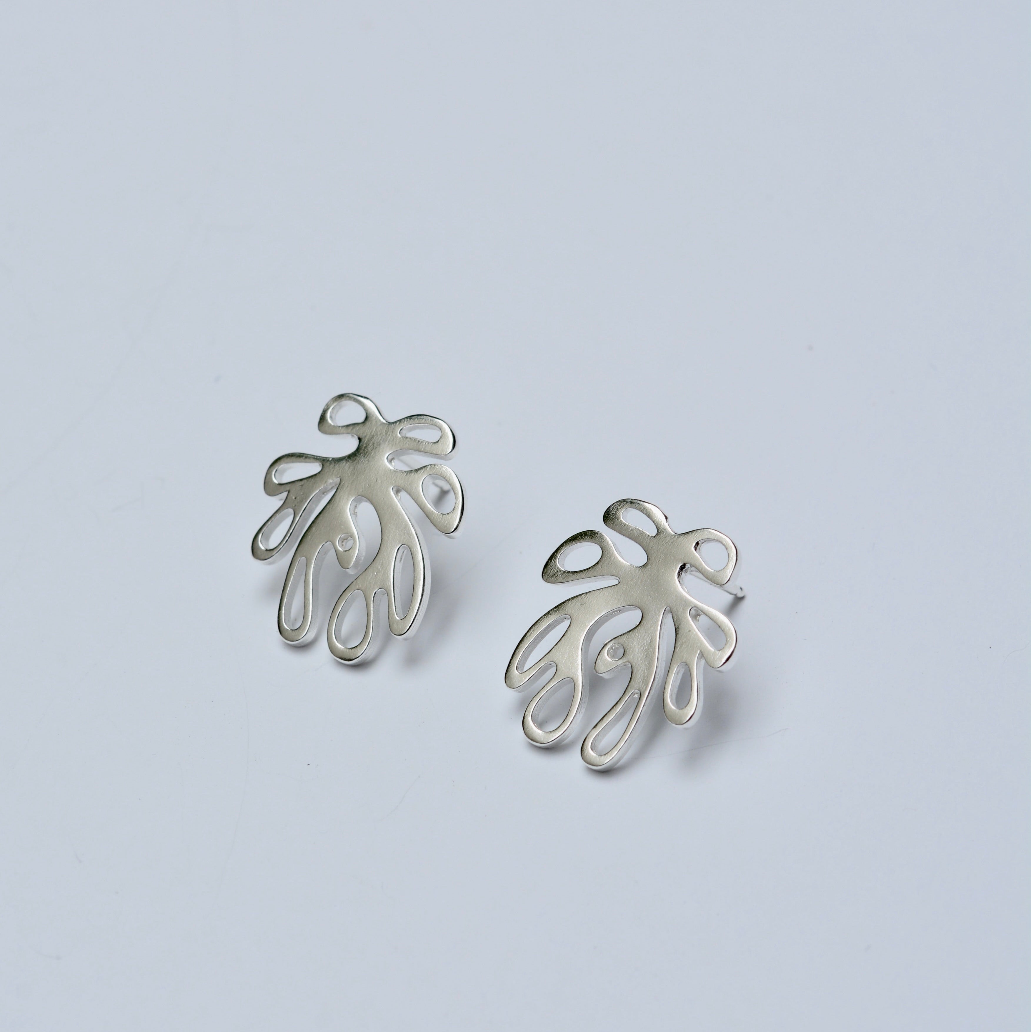 Pair of silver leaf-shaped earrings on a light gray background
