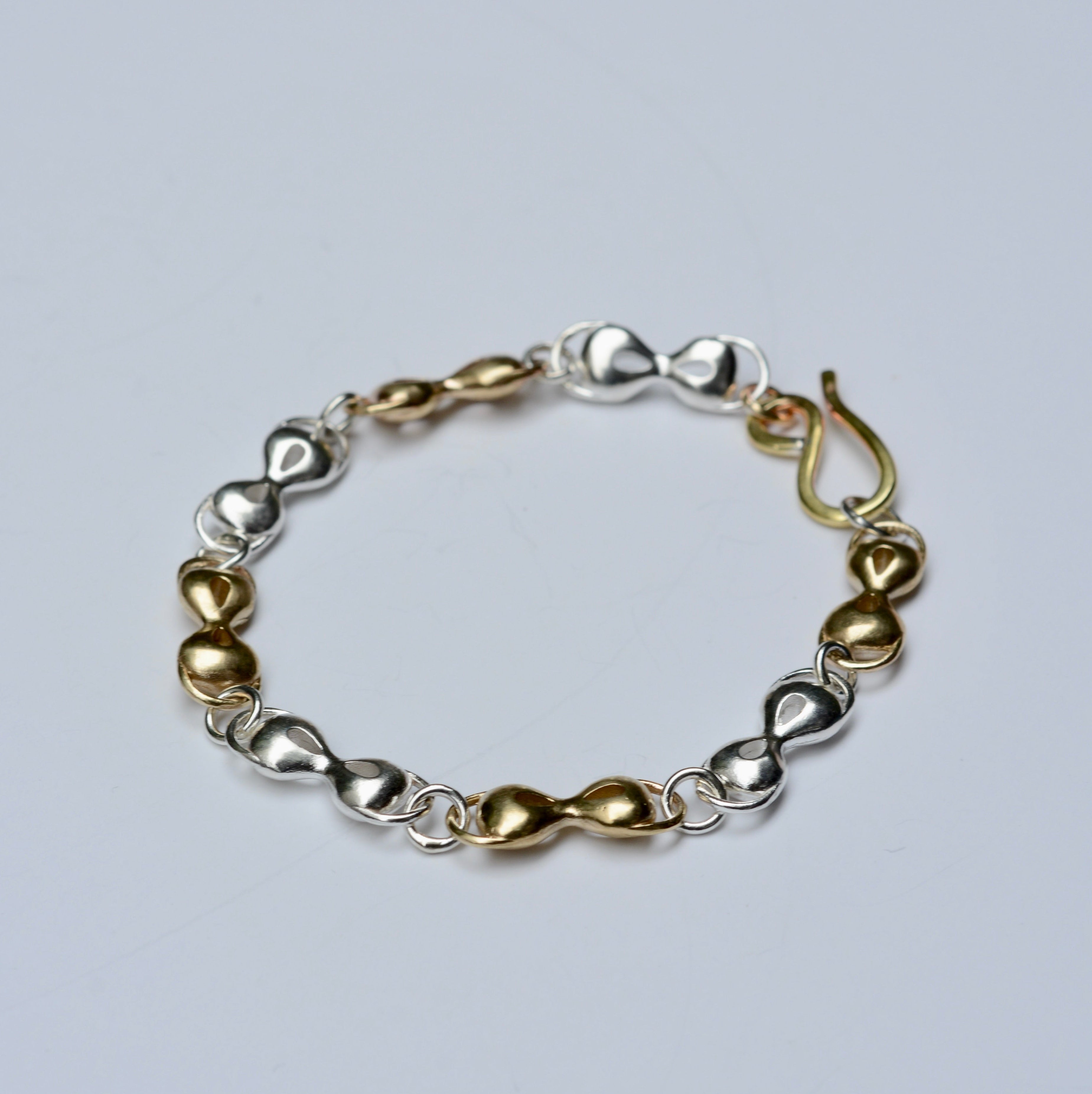 Bracelet with gold and silver mask shaped links on a light gray background