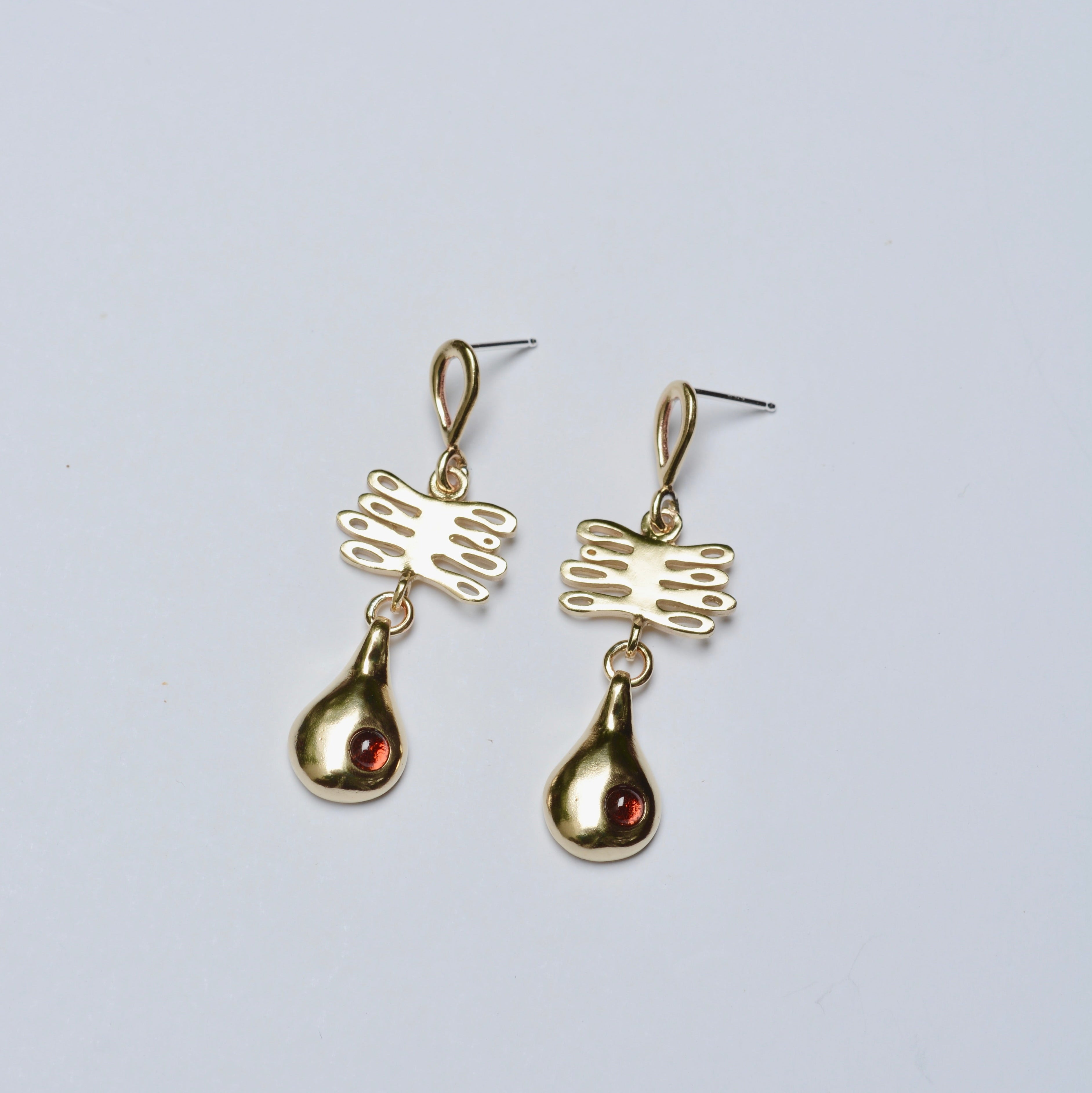 Gold earrings with plant and teardrop shapes on a light gray background