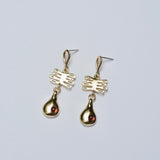 Gold earrings with plant and teardrop shapes on a light gray background