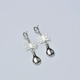 Pair of silver earrings with a plant shaped charm and light blue gemstone on a gray background