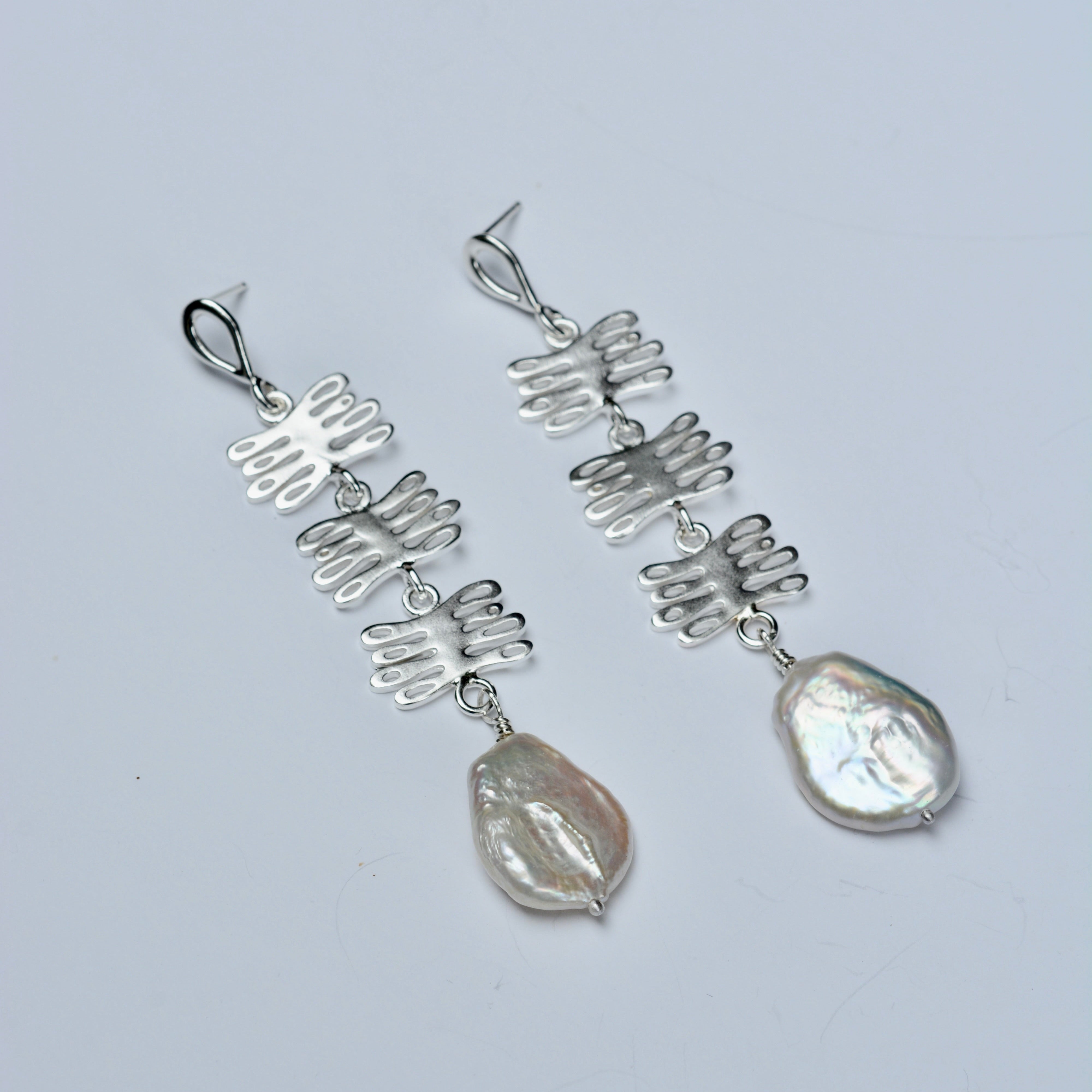 Silver earrings with plant shaped charms and pearls on a light gray background