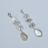 Silver earrings with plant shaped charms and pearls on a light gray background