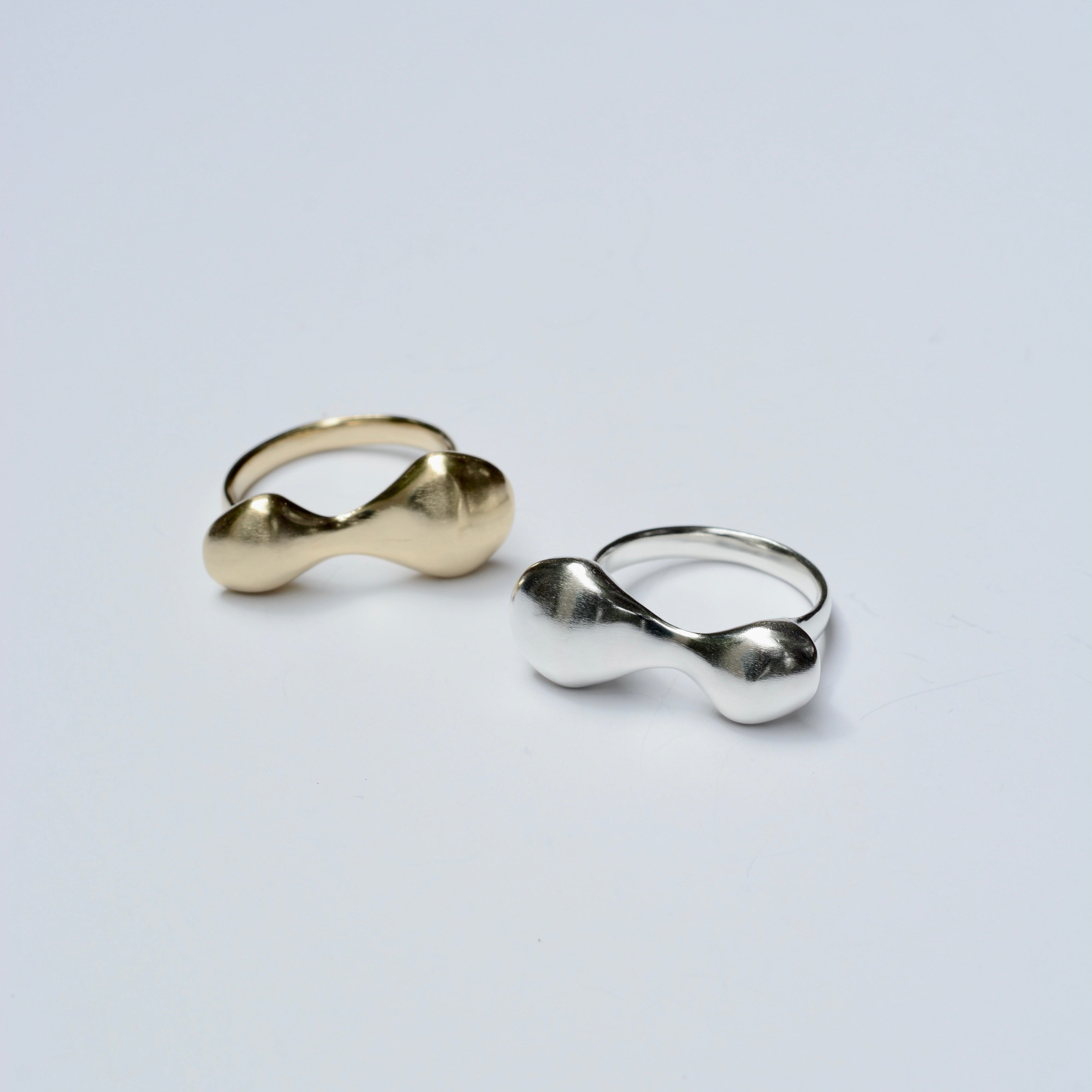 Two rings with organic blobby shapes, one bronze and one silver, on a light gray background