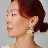 Woman wearing a pair of silver leaf shaped earrings against a neutral background