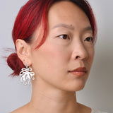 Woman with red hair wearing a silver coral shaped dangle earring against a plain background