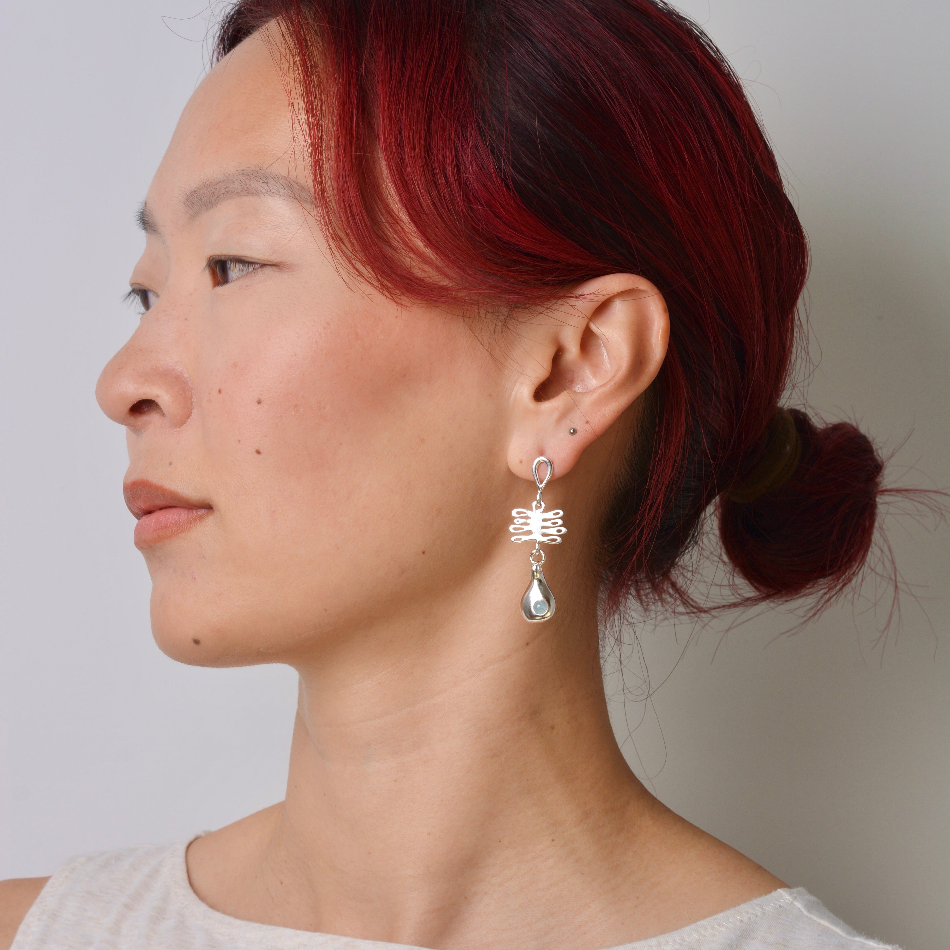 Woman with red hair wearing a silver earring against a plain background