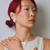 Woman with red hair wearing coral shaped post earrings and rings, against a plain background