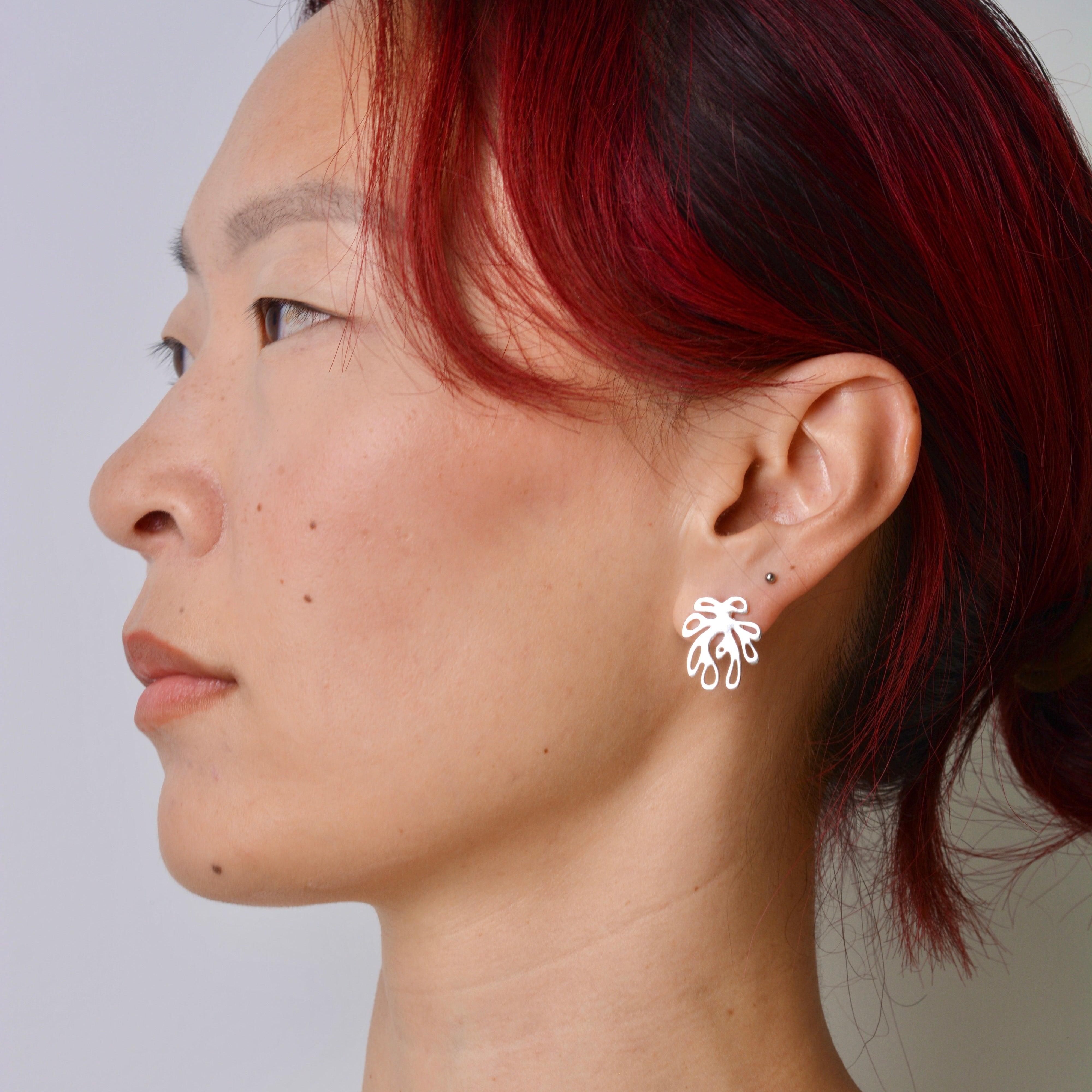 Person wearing a silver coral shaped earring with a white background