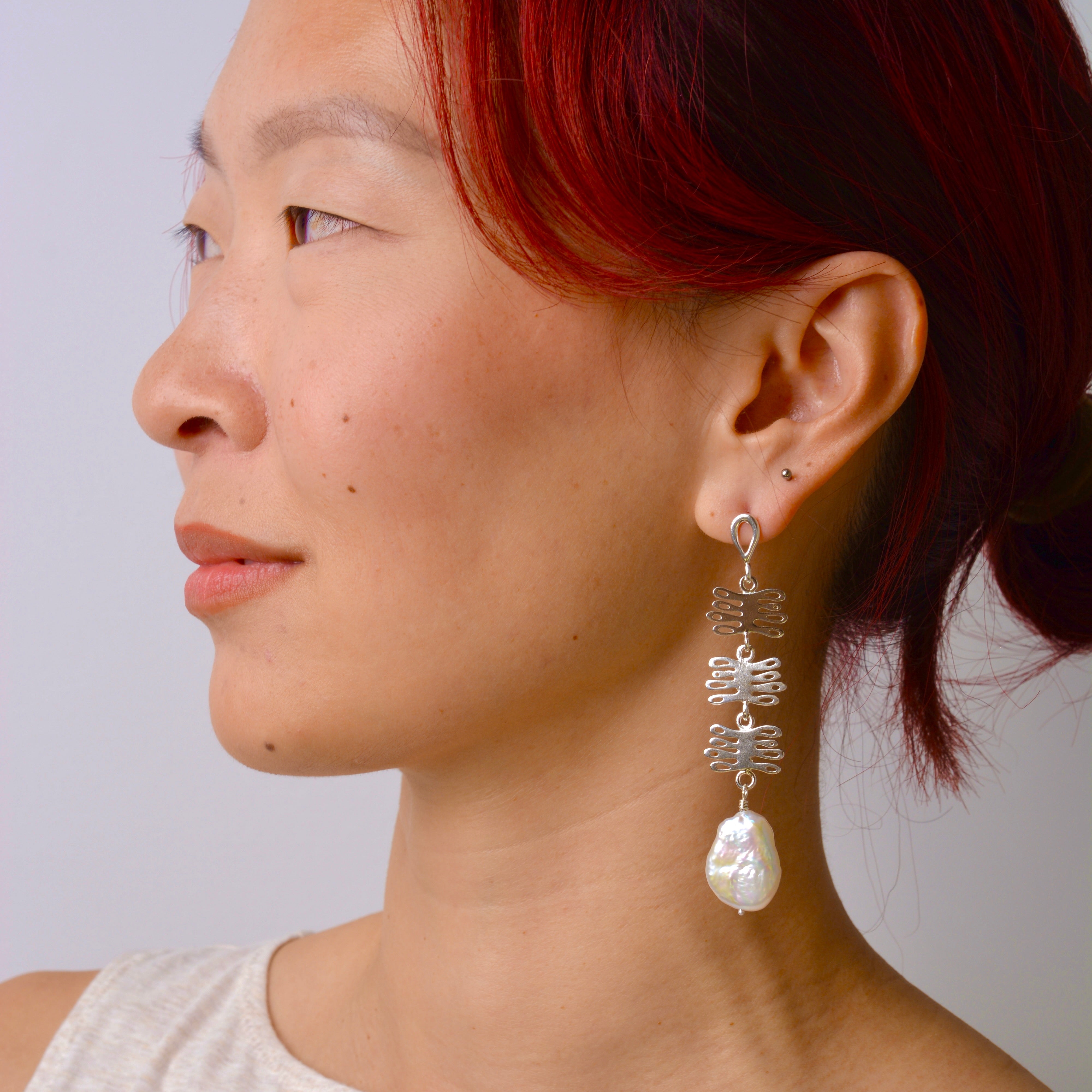Woman wearing a silver earring with a pearl drop against a plain background