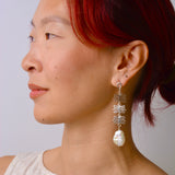 Woman wearing a silver earring with a pearl drop against a plain background