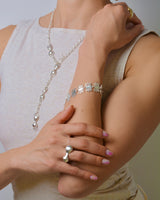 Person wearing silver jewelry including a necklace, bracelet, and rings on a neutral background