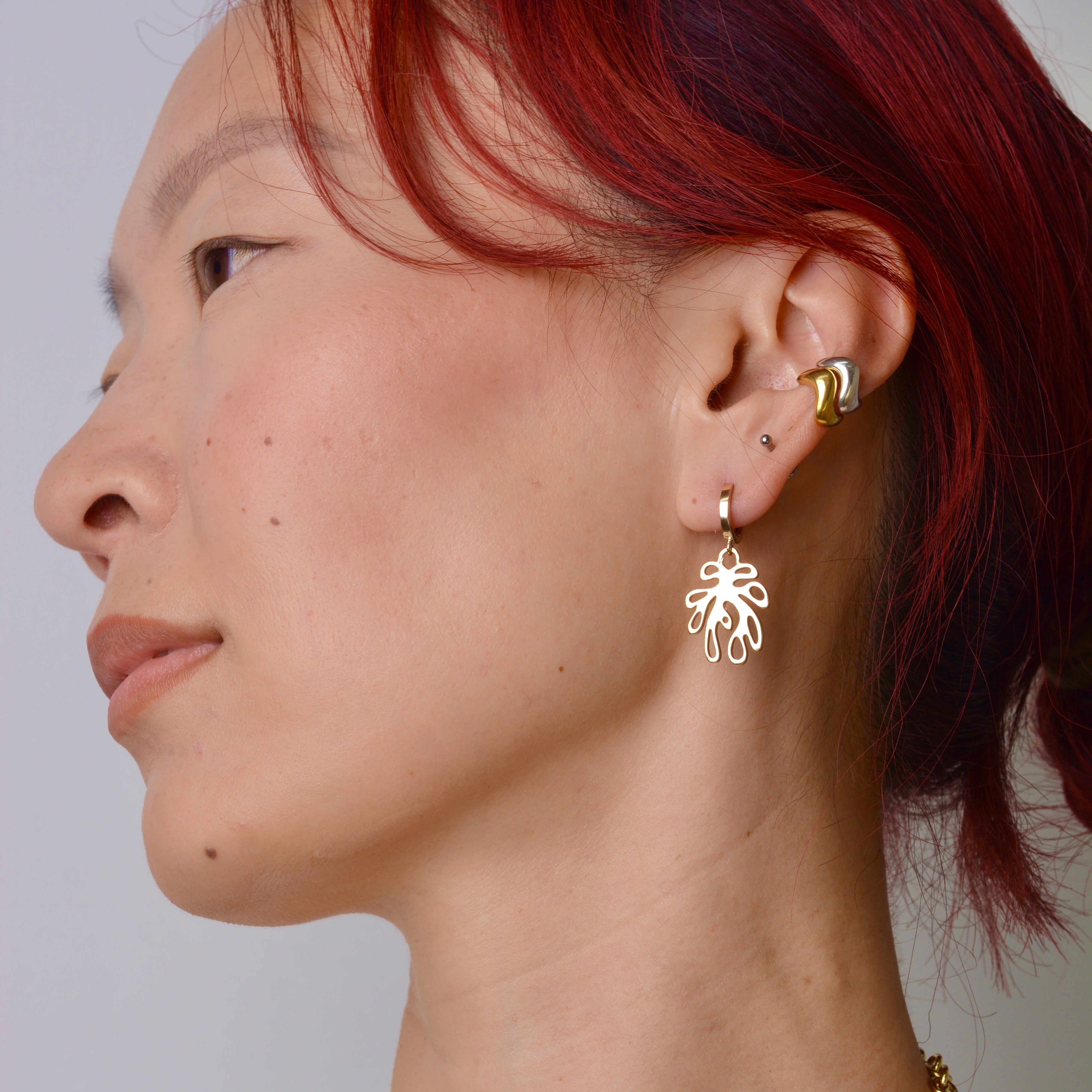 Woman wearing bronze plant shaped huggie earrings against a plain background