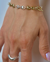 Hand wearing a bronze and silver bracelet with a silver ring on a neutral background