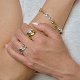 Close-up of a hand wearing multiple wavy stacking rings and a bracelet on a light background