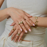 Close-up of hands wearing bronze and silver rings and bracelets on a neutral background