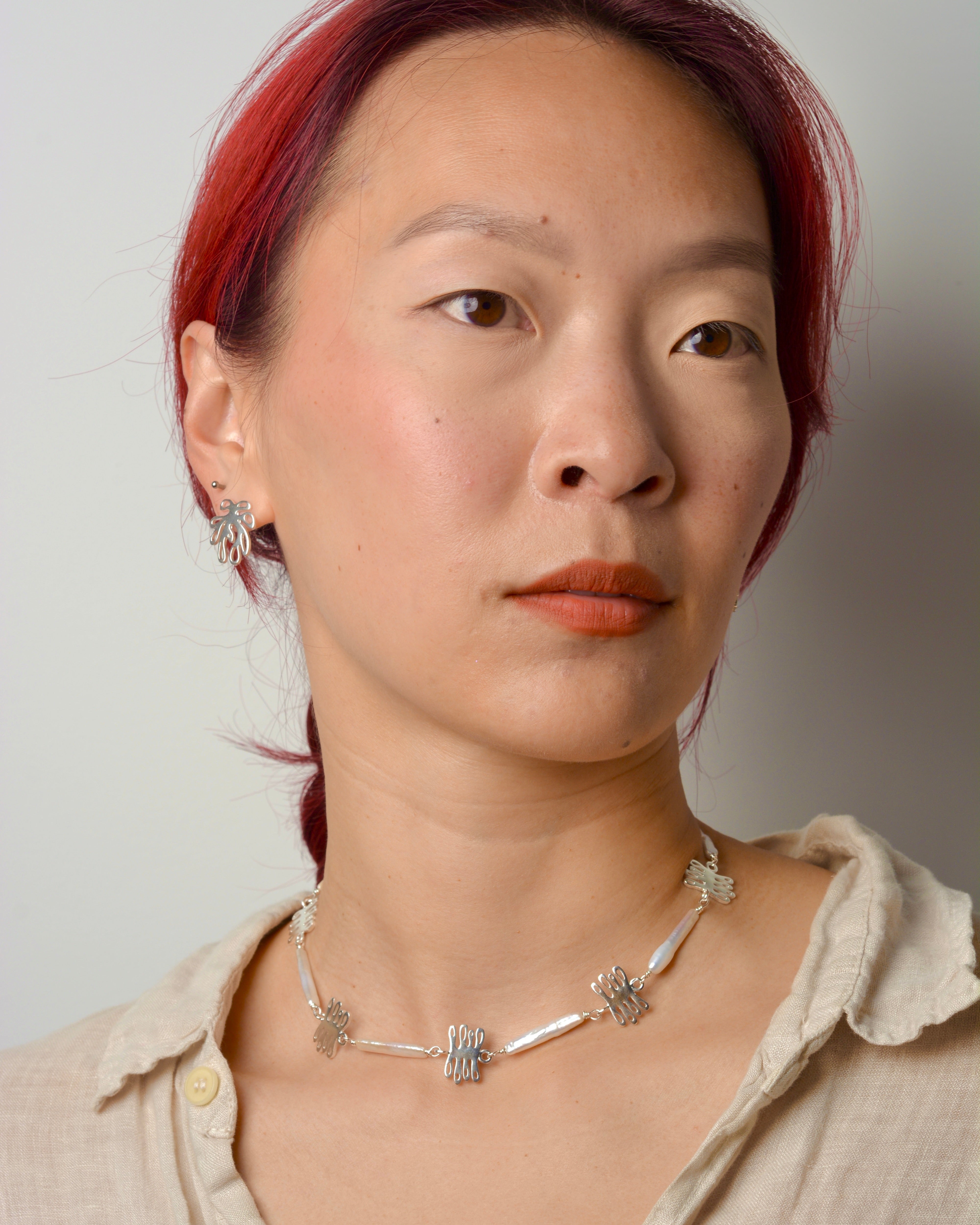 Woman with red hair wearing a pearl and charm necklace against a plain background