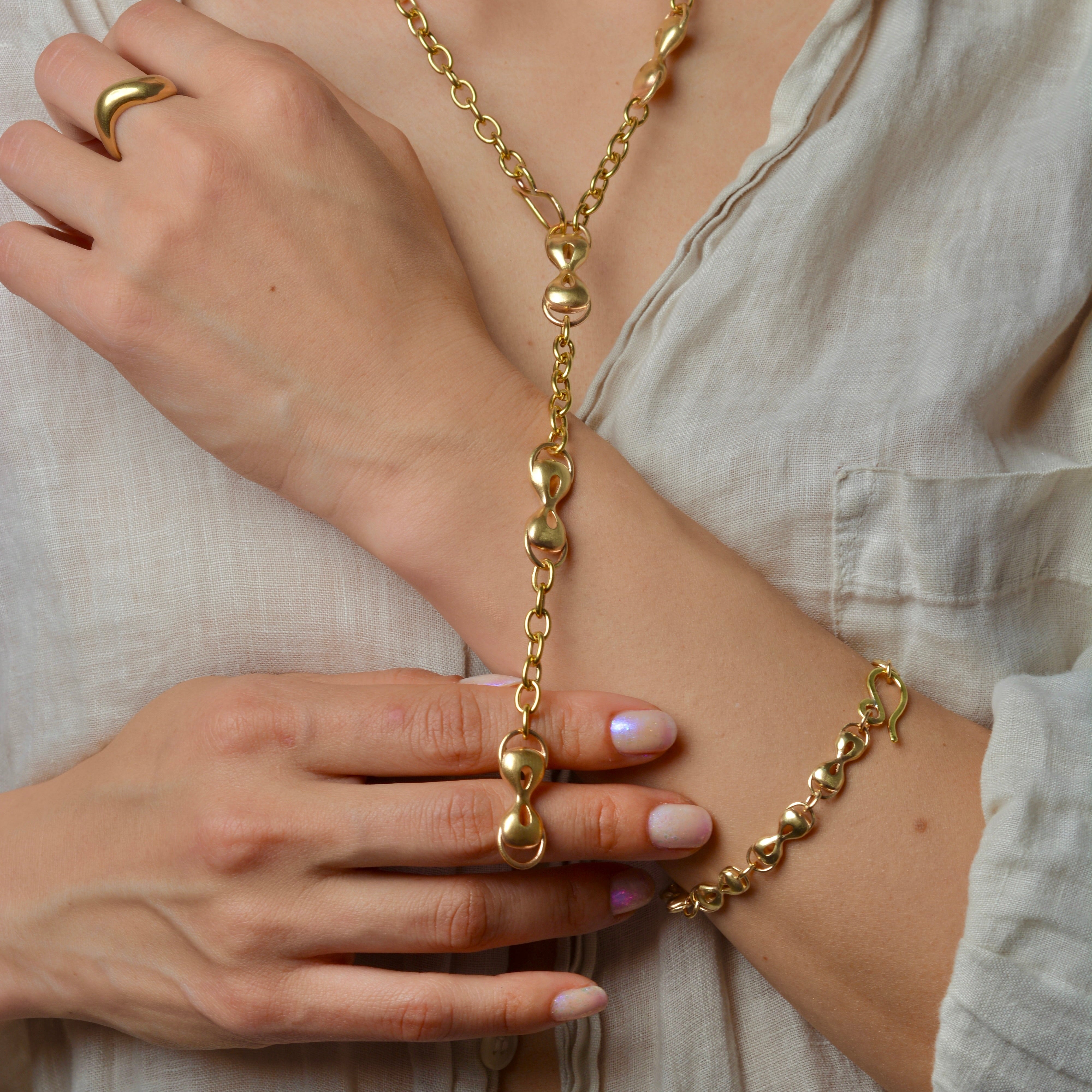 Person wearing a bronze chain necklace and bracelet, with a neutral background