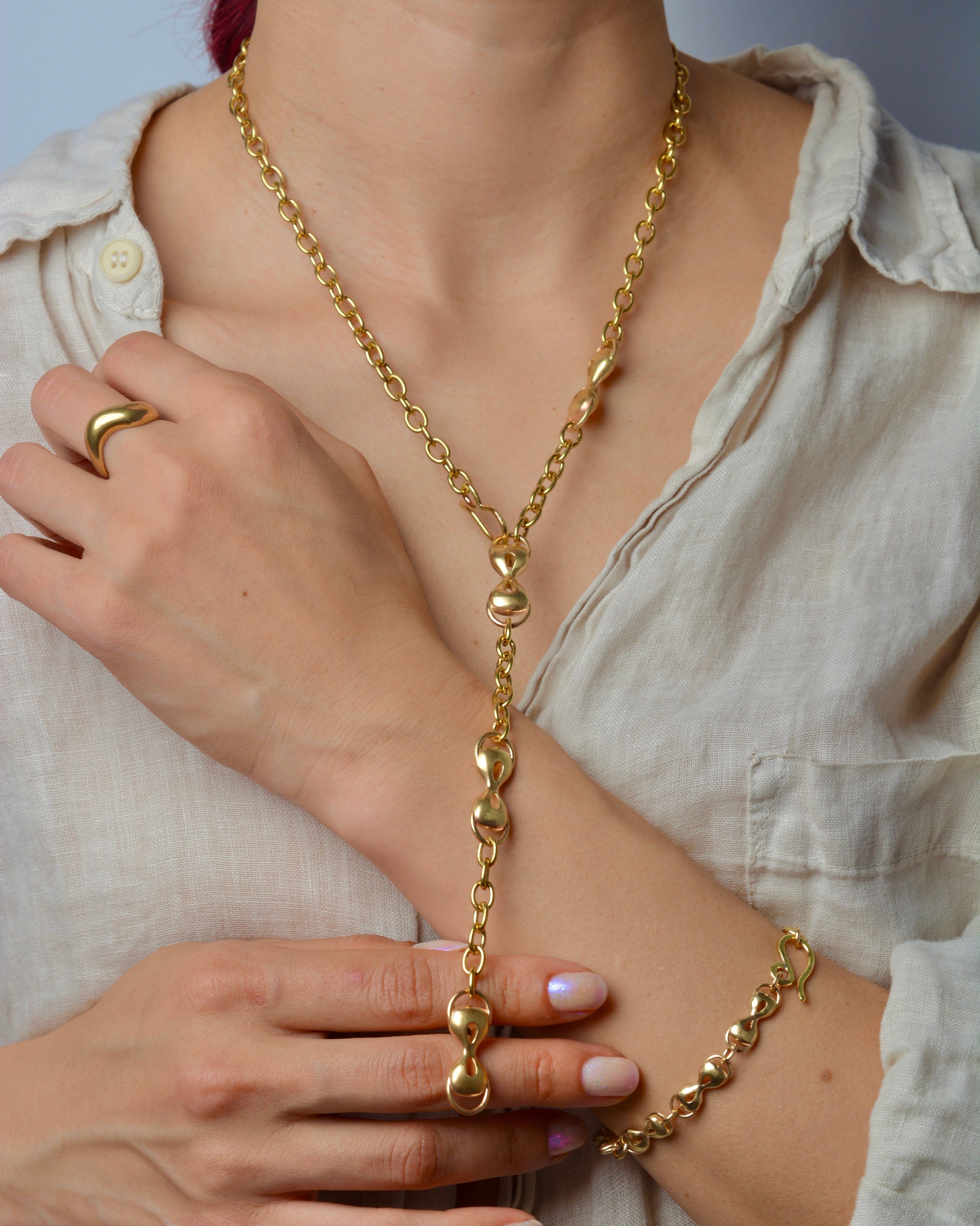 Person wearing a bronze chain necklace and bracelet, with a neutral background