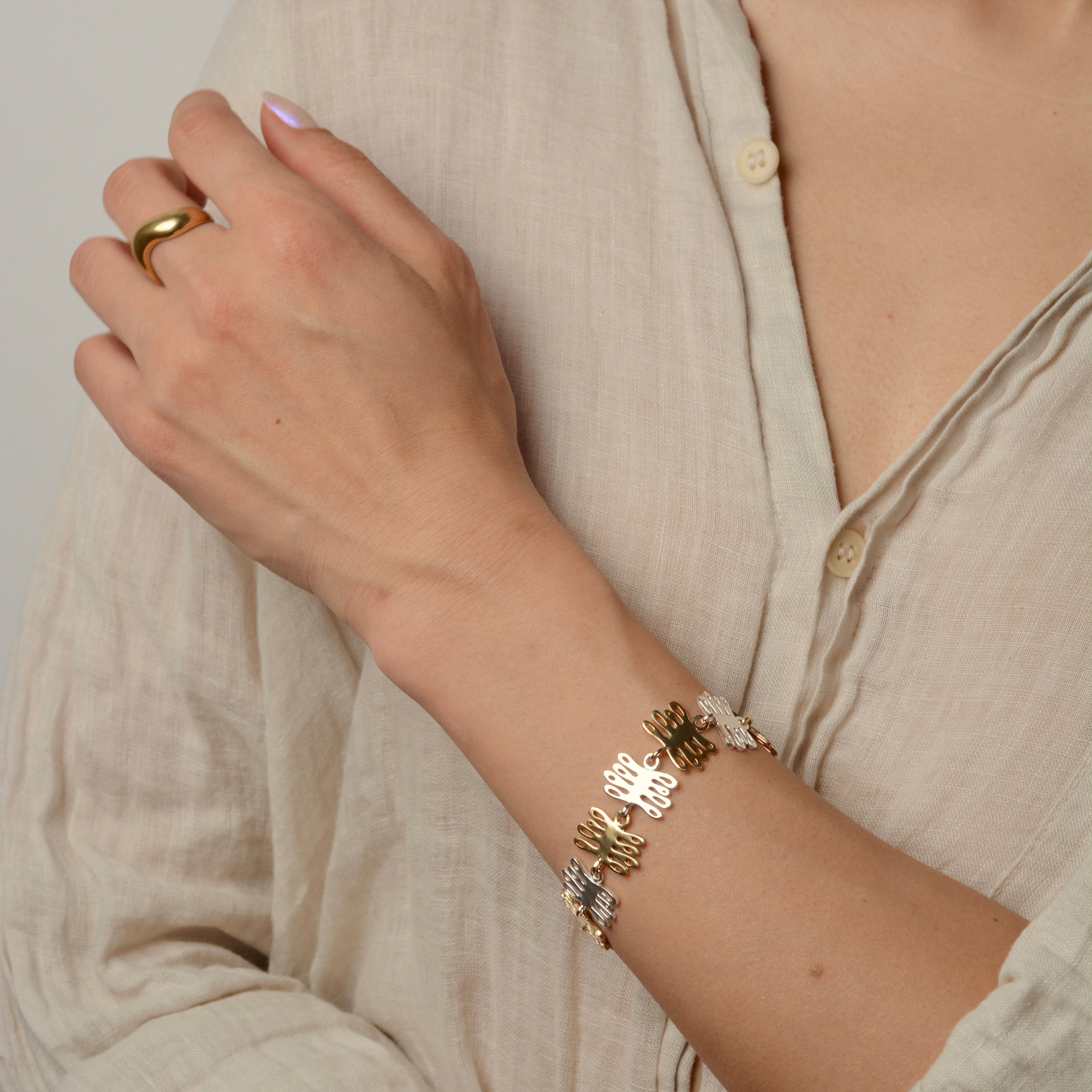 Person wearing a mixed metal plant inspired bracelet and bronze wavy ring on a neutral background