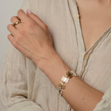 Person wearing a mixed metal plant inspired bracelet and bronze wavy ring on a neutral background
