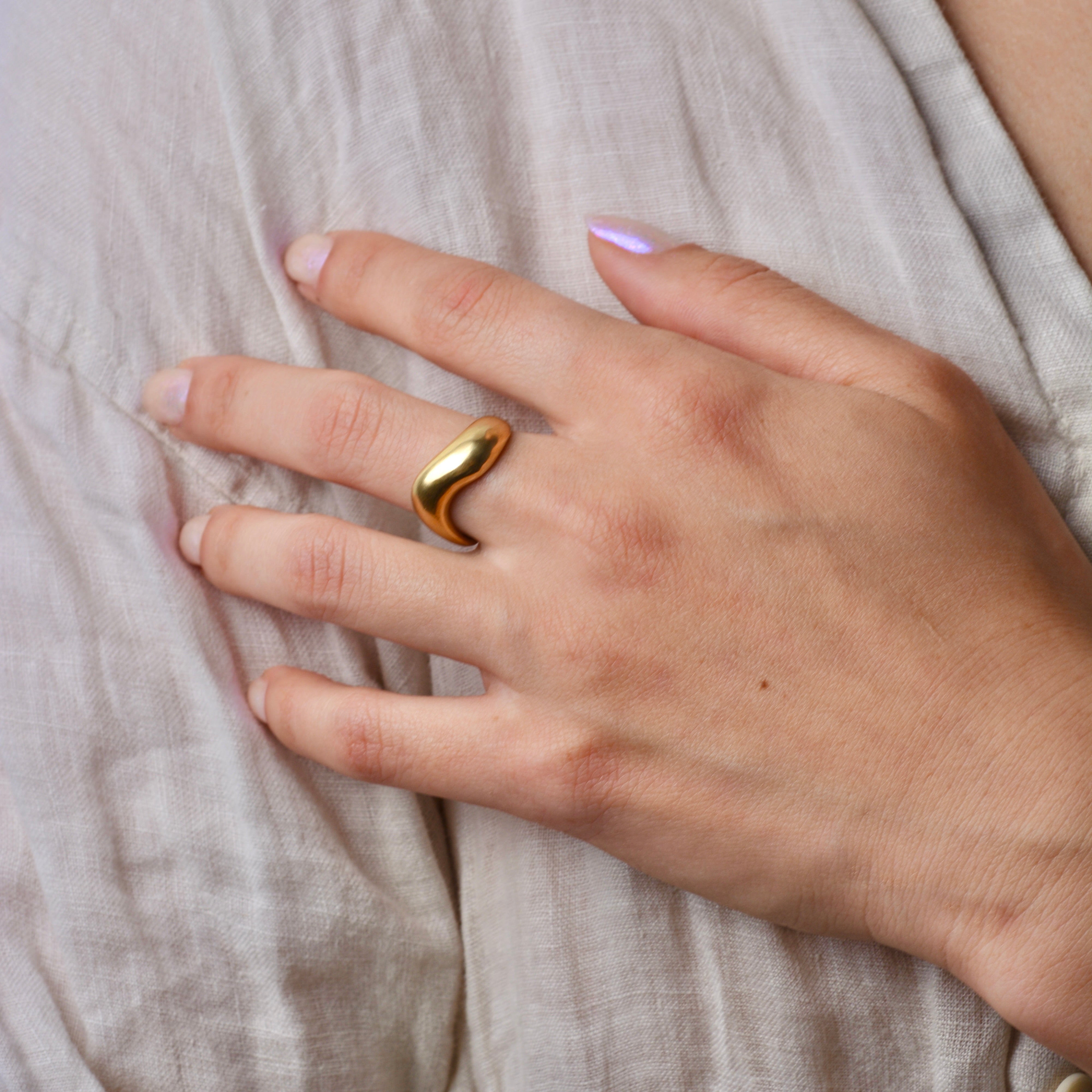 Hand wearing an organic, wavy bronze ring on beige fabric