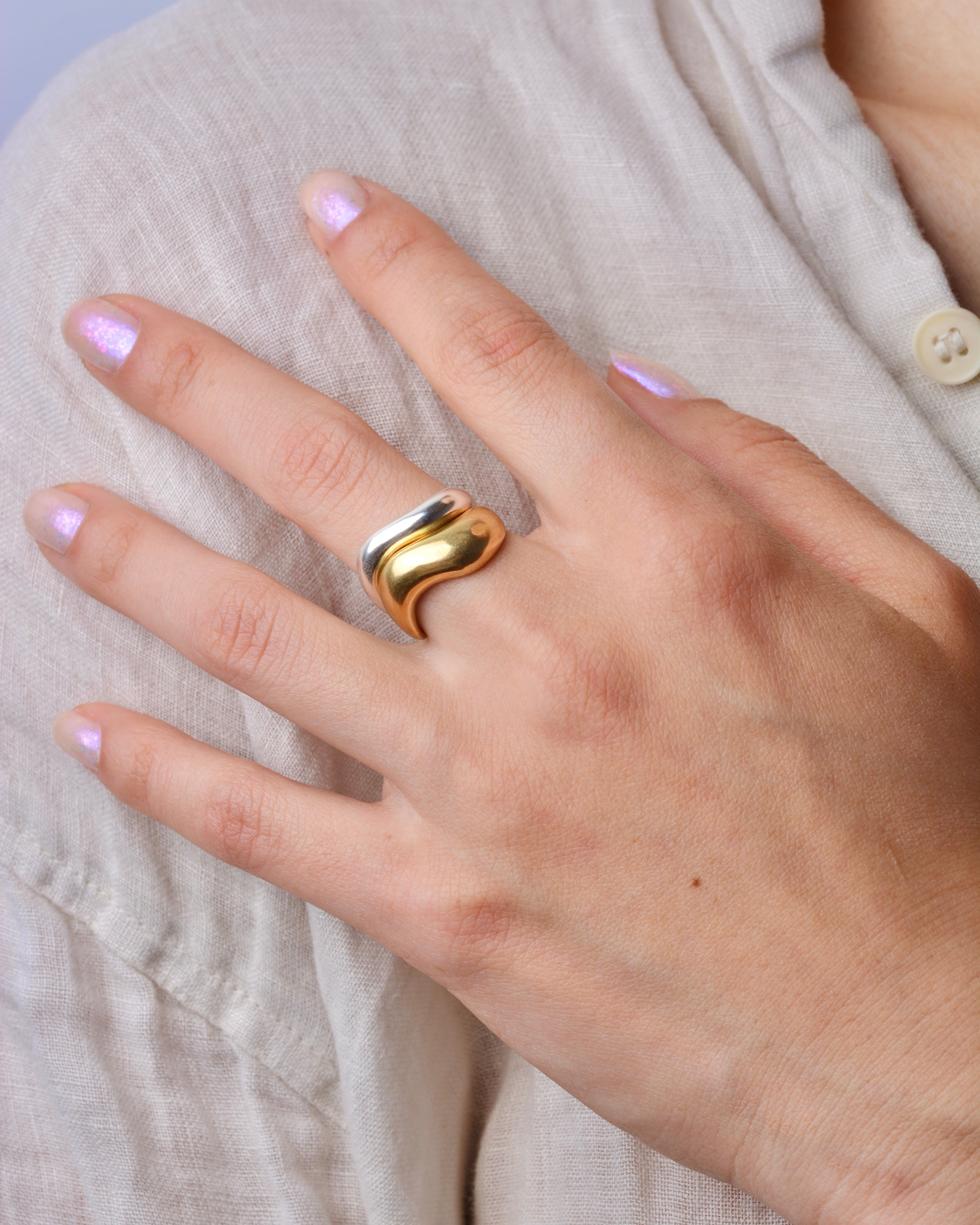 Hand wearing a bronze wavy ring stacked with a silver ring on with a light-colored shirt background
