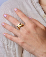 Hand wearing a bronze wavy ring stacked with a silver ring on with a light-colored shirt background