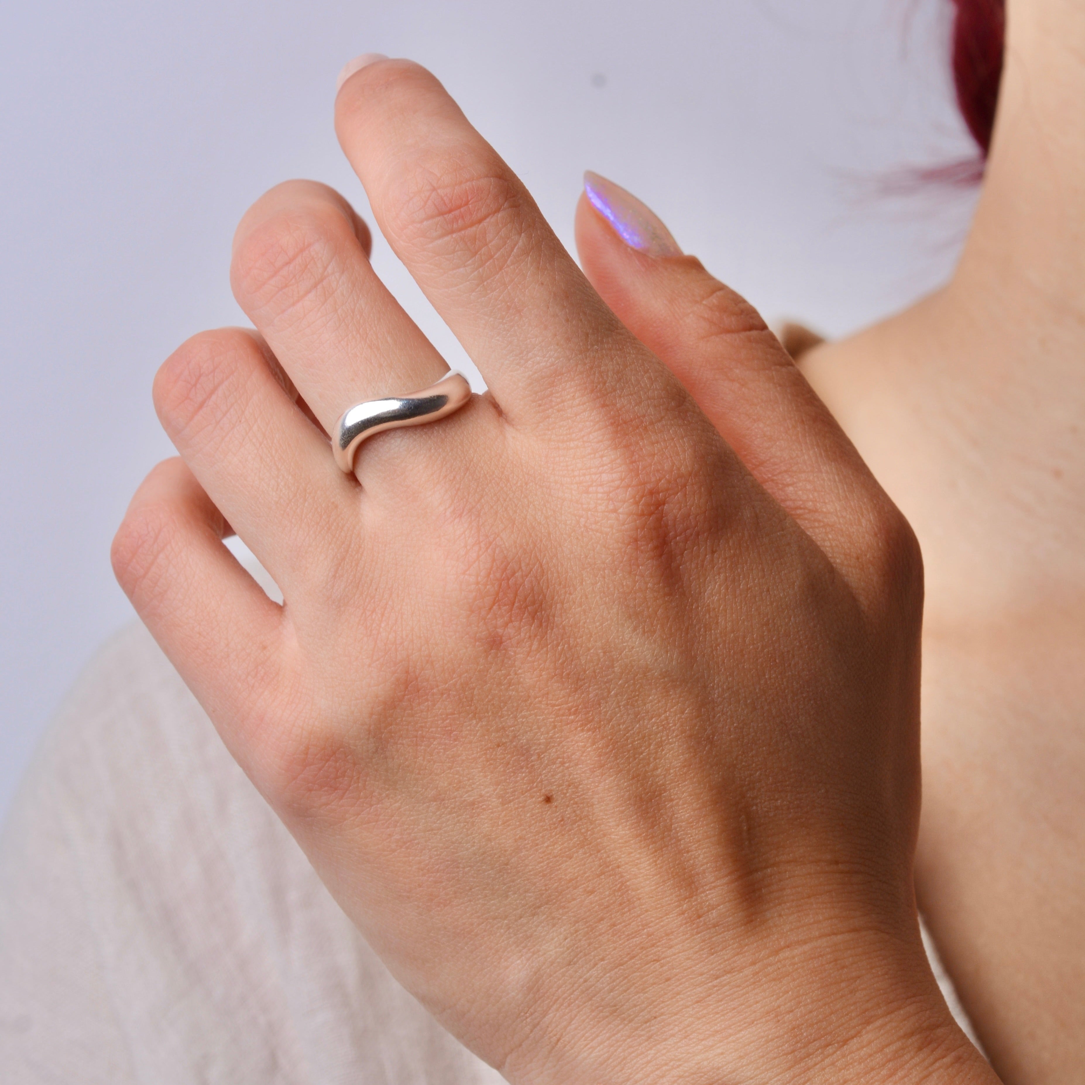 Close-up of a hand wearing a silver wavy organic ring with a plain background