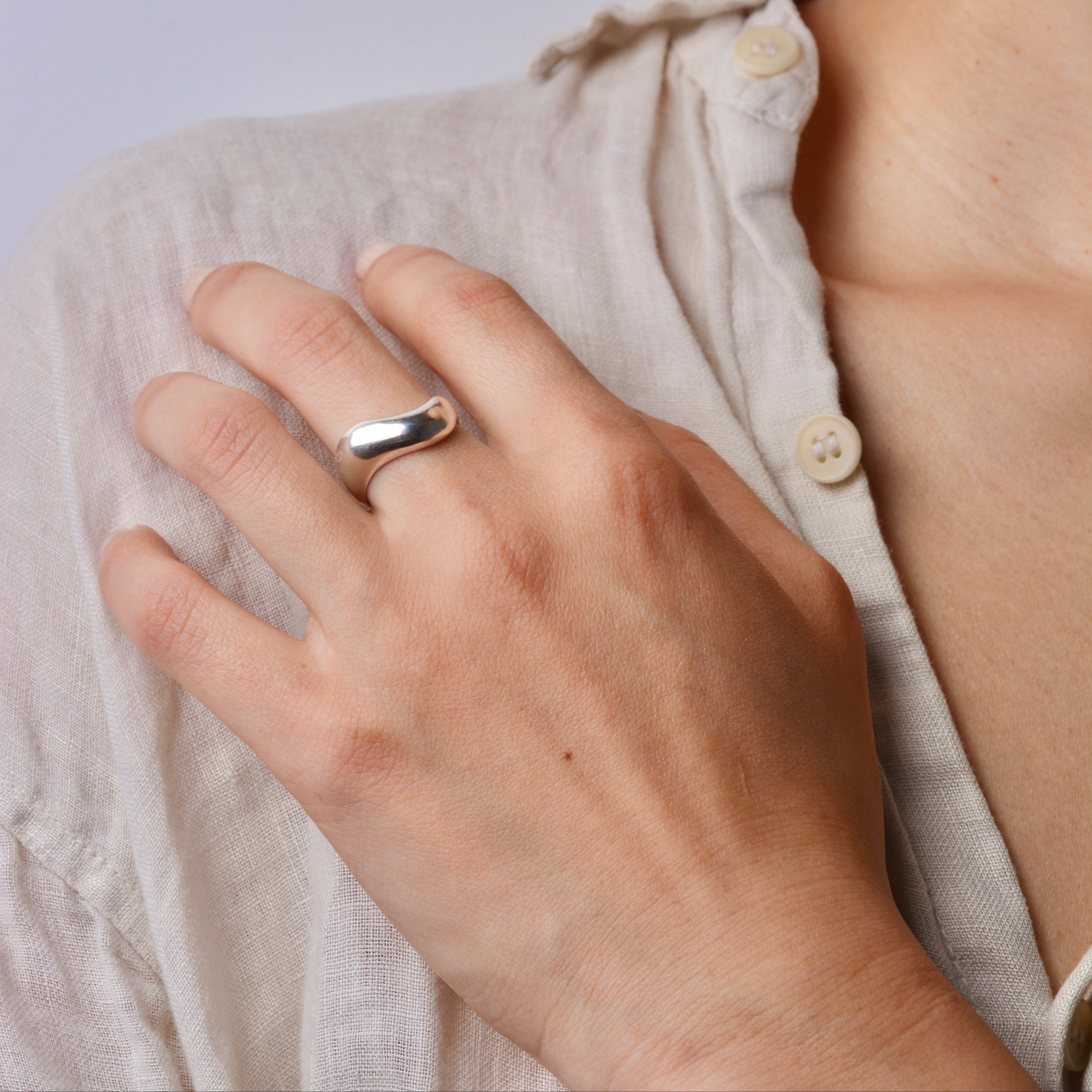 Close-up of a hand wearing a wide wavy silver ring on a shoulder