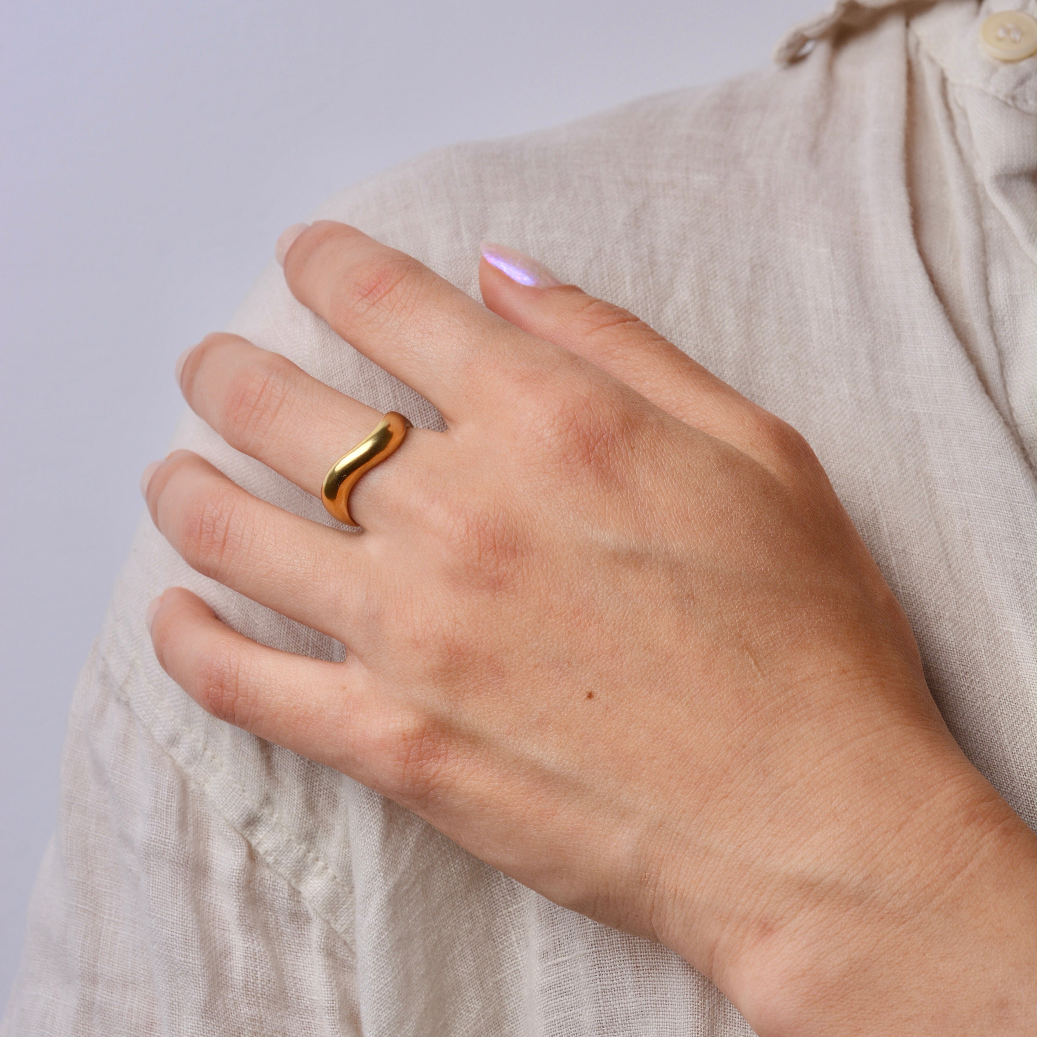 Hand wearing a bronze wavy ring on a light background