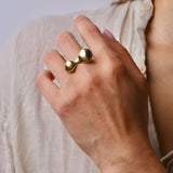 Hand wearing a gold blob shaped ring with a plain background