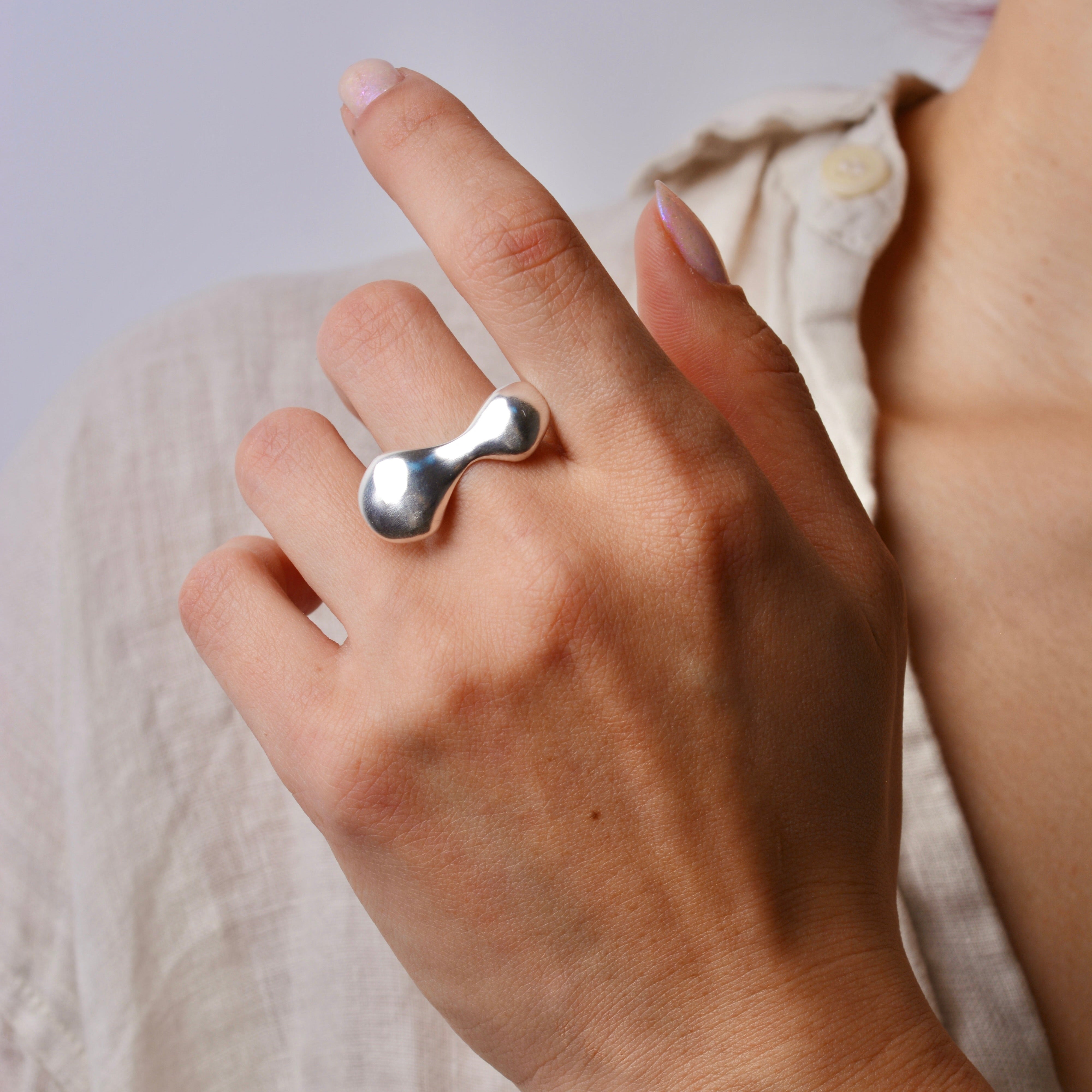 Hand wearing a silver organic ring with a plain background