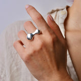 Hand wearing a silver organic ring with a plain background