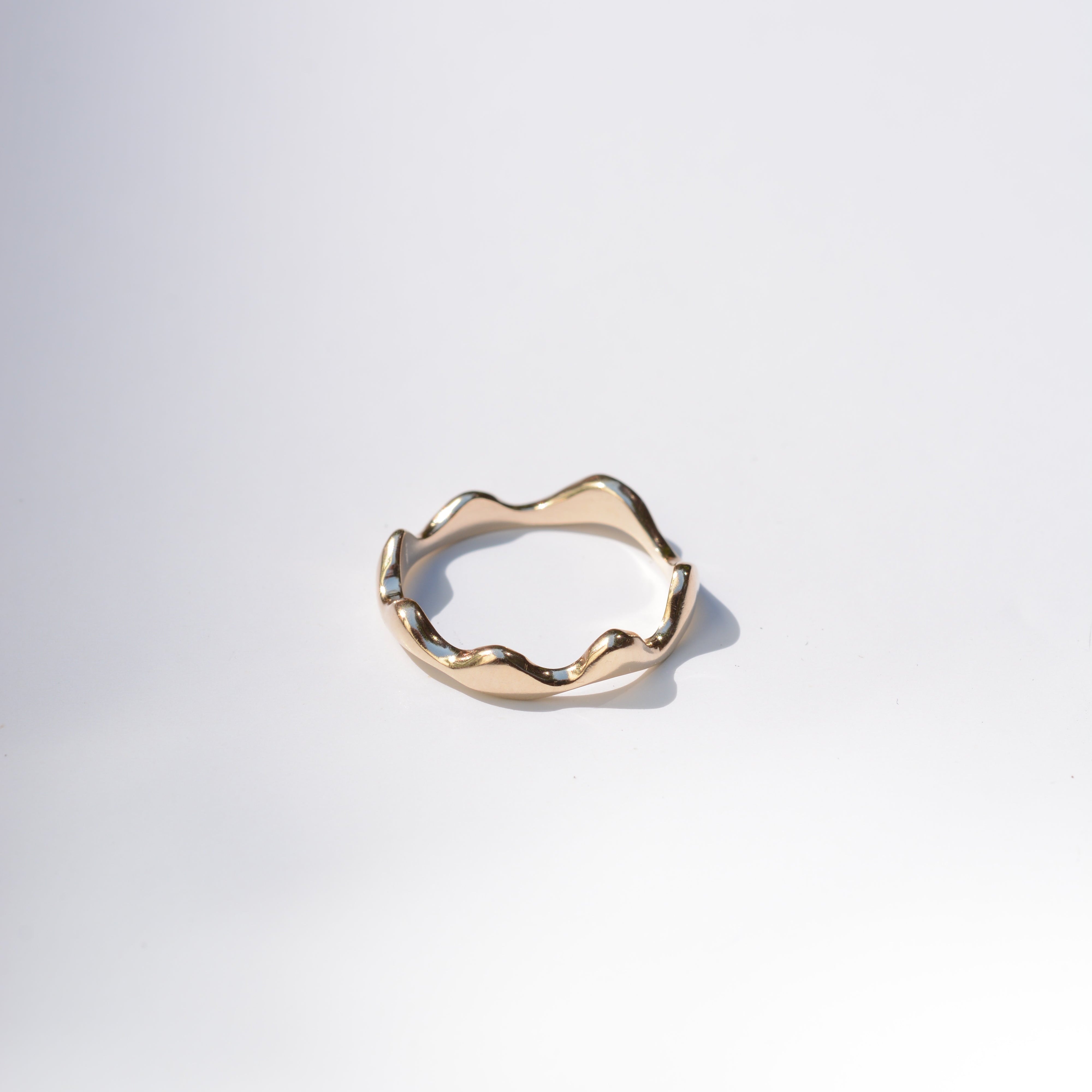 A single gold ring with a wavy, organic textured band, photographed on a clean white background with a soft shadow.
