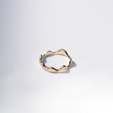 A single gold ring with a wavy, organic textured band, photographed on a clean white background with a soft shadow.