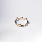 A single gold ring with an organic, wavy, undulating band design, photographed on a clean white background with a soft shadow.