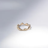 A single gold ring with an organic, wavy, undulating band design, photographed on a clean white studio background with soft shadows.