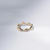 A gold ring with an organic, wavy, undulating band, photographed on a clean white studio background.