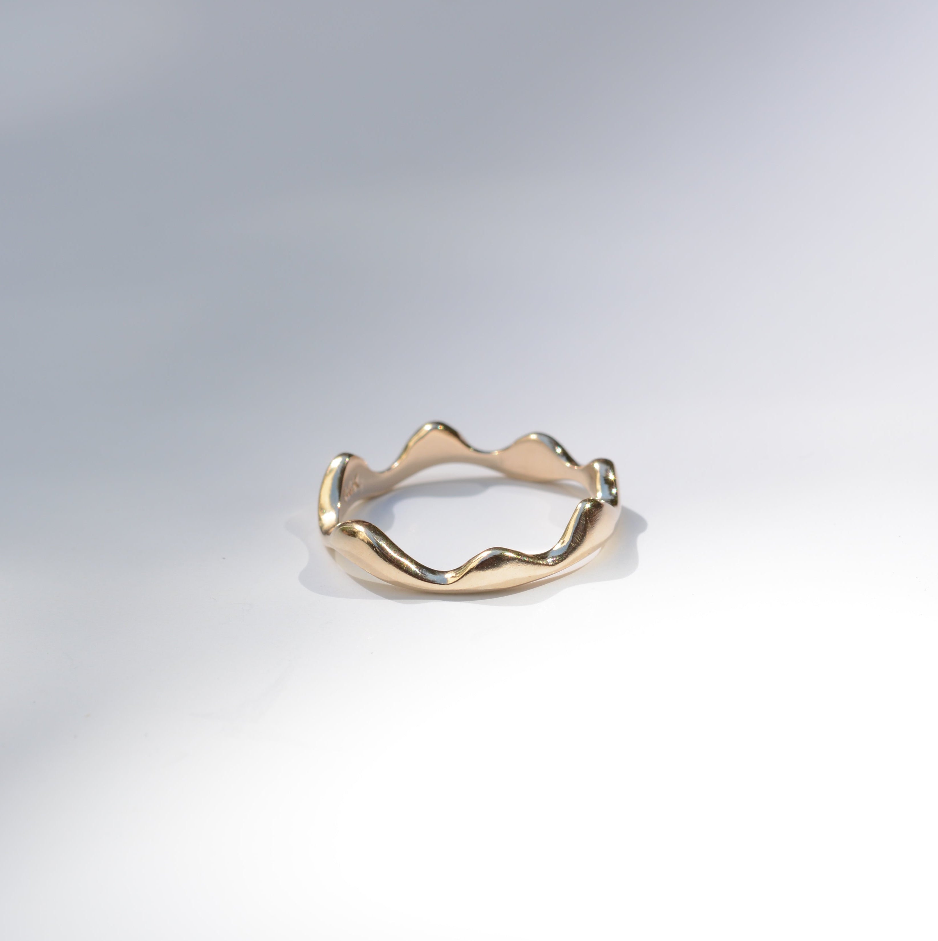 A gold ring with an organic, wavy, mountain-like silhouette, photographed on a clean white studio background with soft shadows.