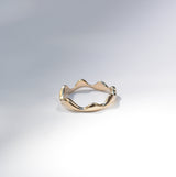 A gold ring with an organic, wavy, mountain-like silhouette, photographed on a clean white studio background with soft shadows.