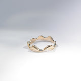 A gold wavy band ring with a scalloped, undulating edge, photographed on a clean white surface with soft shadows.