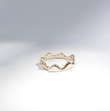 A thin gold ring with a wavy, undulating edge, photographed on a clean white surface with soft shadows.