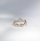 A single gold ring with a wavy, organic textured band, photographed on a clean white studio background with soft shadows.