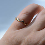 A close-up of a hand wearing a thin, wavy gold ring against a soft, light blue background.