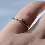 A close-up of a hand wearing a thin, wavy gold ring against a soft, light blue background.