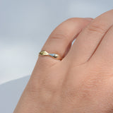 A close-up of a hand wearing a thin, polished gold ring with a unique wavy, organic shape against a soft, light blue-gray background.