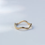 A thin, wavy gold ring with a unique undulating band, photographed on a clean white surface with soft, natural-looking shadows.