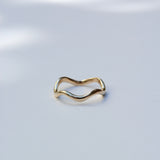 A thin, wavy gold band ring photographed on a clean white surface with soft shadows.