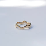 A single gold wavy band ring photographed on a clean white surface with soft natural shadows.